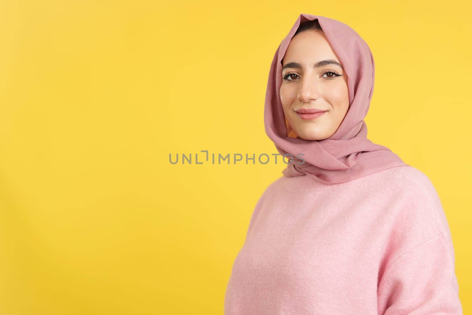 Happy muslim woman wearing hijab looking at the camera in studio with yellow background