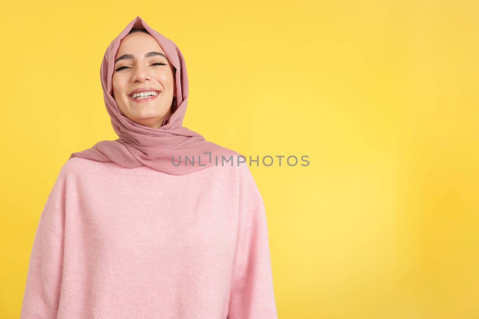 Beauty young muslim woman wearing hijab smiling in studio with yellow background