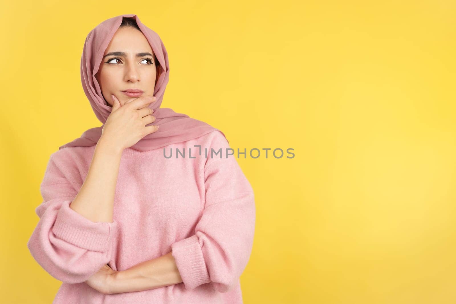 Muslim woman with hand on face and thoughtful expression in studio with yellow background