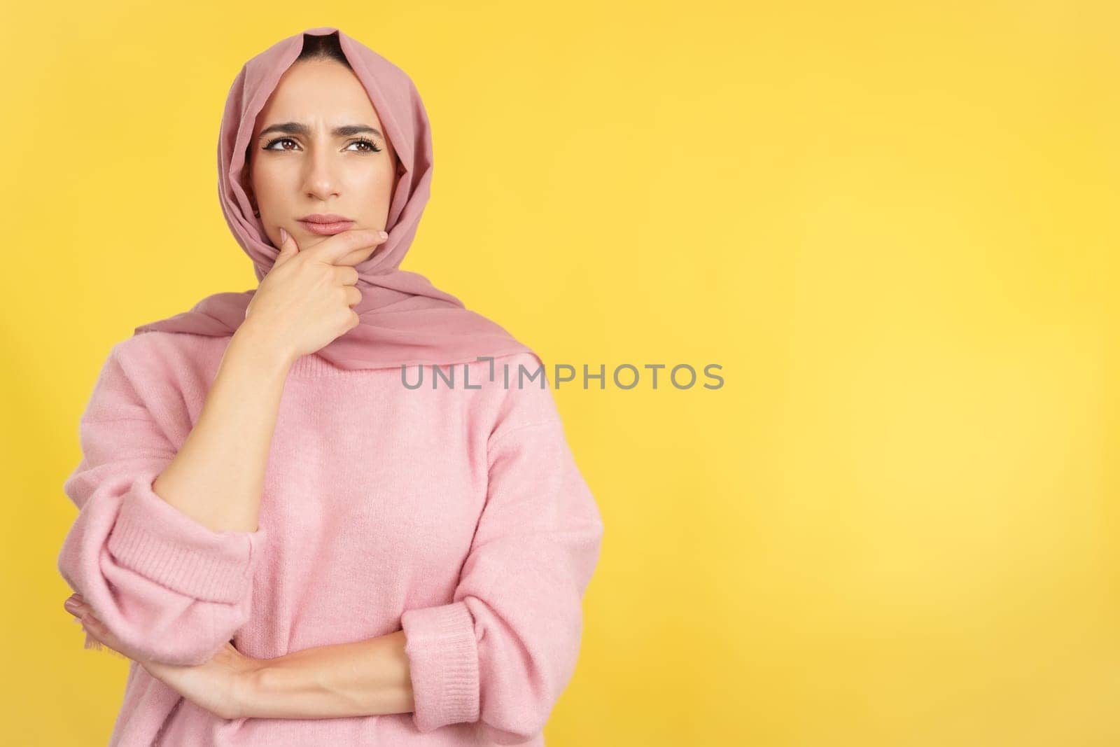 Worried muslim woman looking away with pensive expression in studio with yellow background