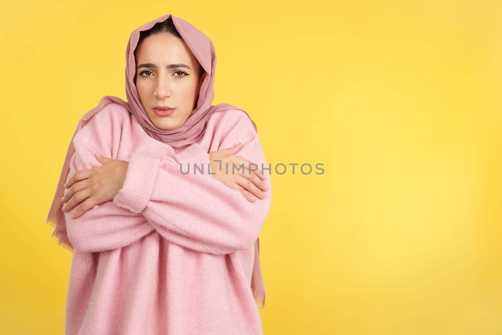 Muslim woman looking at camera in the cold in studio with yellow background