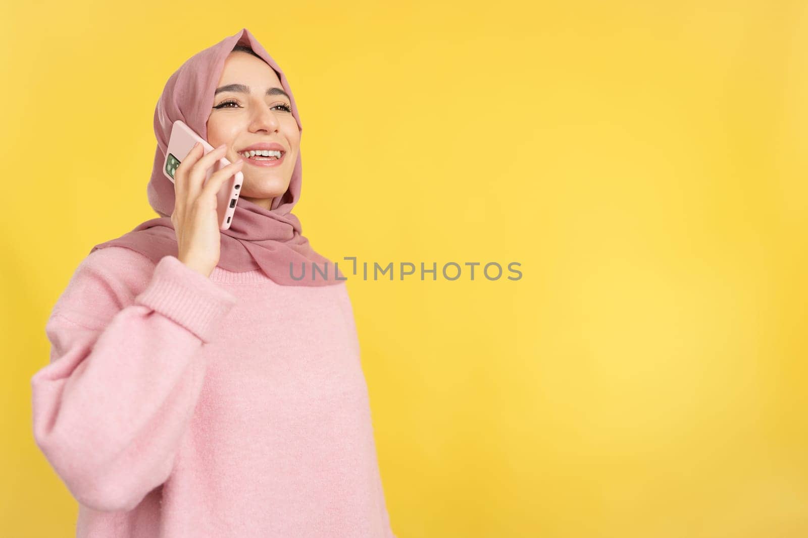 Happy muslim woman talking to the mobile phone in studio with yellow background