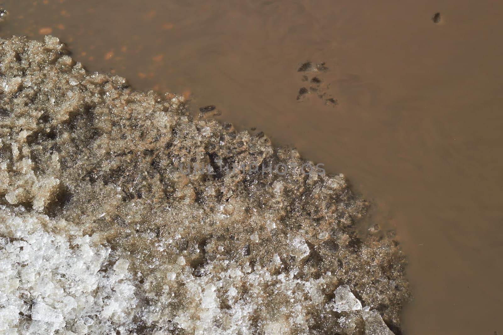 Abstract background of a melted mud puddle and remnants of snow. The color of cocoa. Off-road.