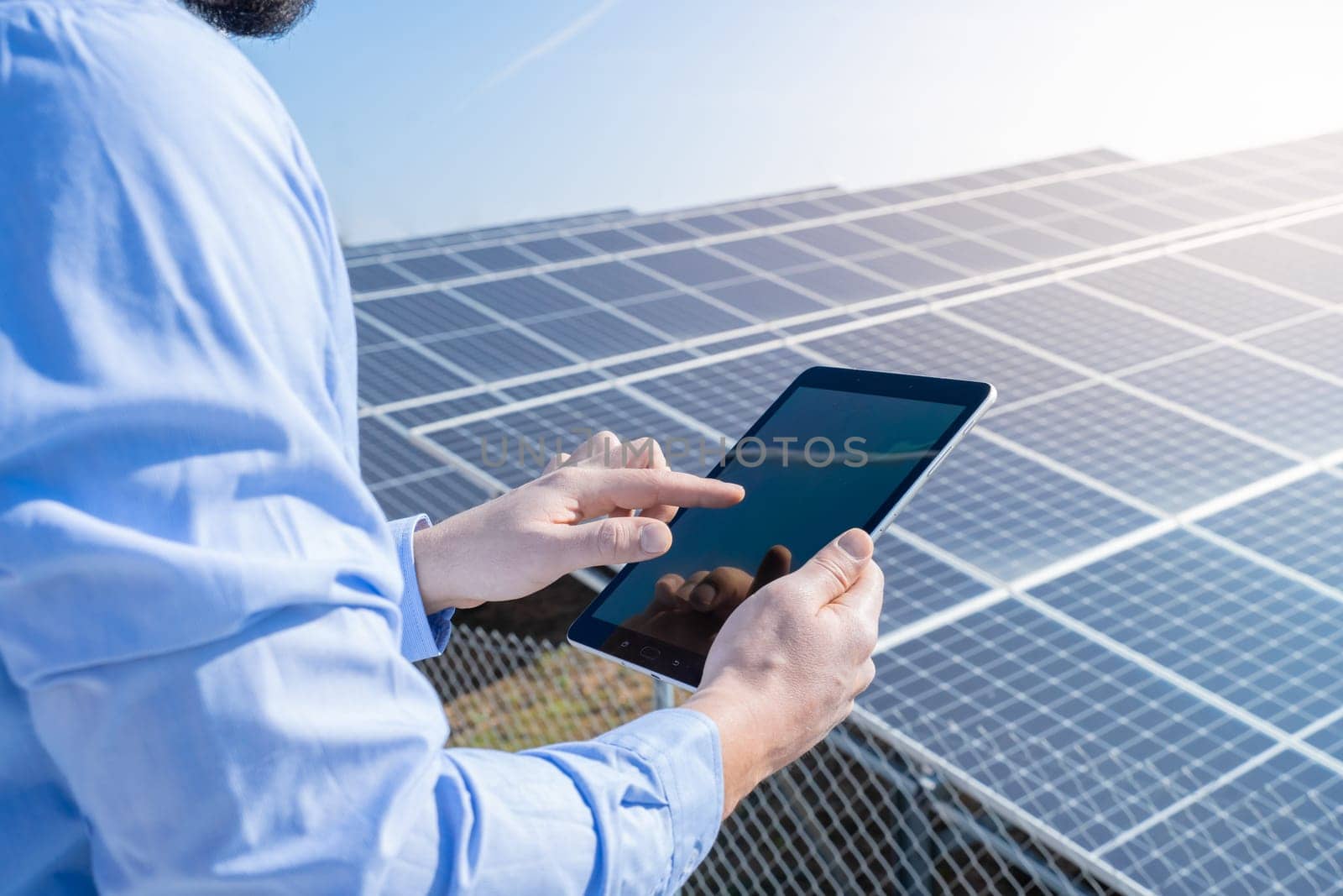 Engineer with a tablet with photovoltaic solar panel system plant in the background. Green clean energy concept.