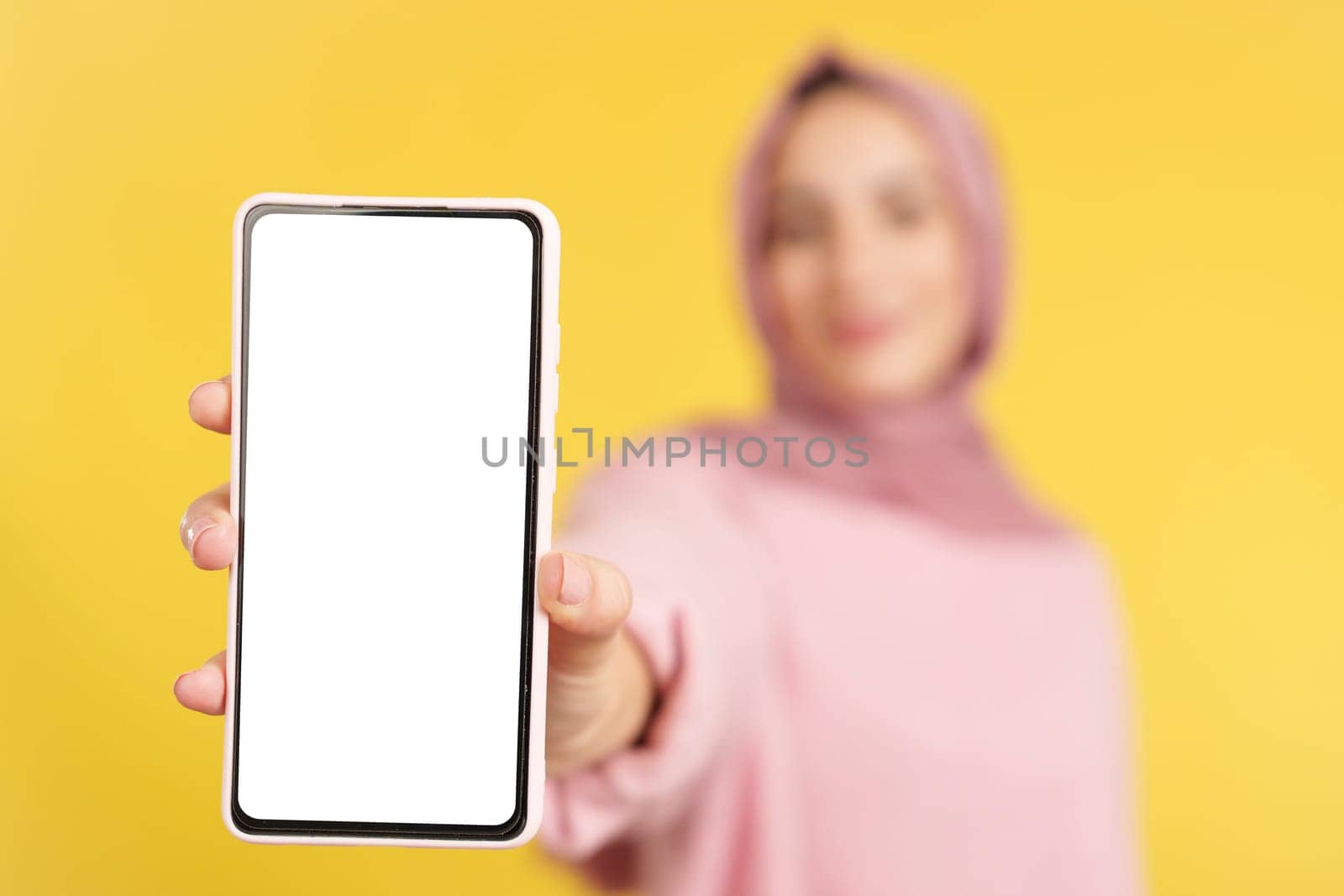 Blank screen of the mobile held by a muslim woman in studio with yellow background