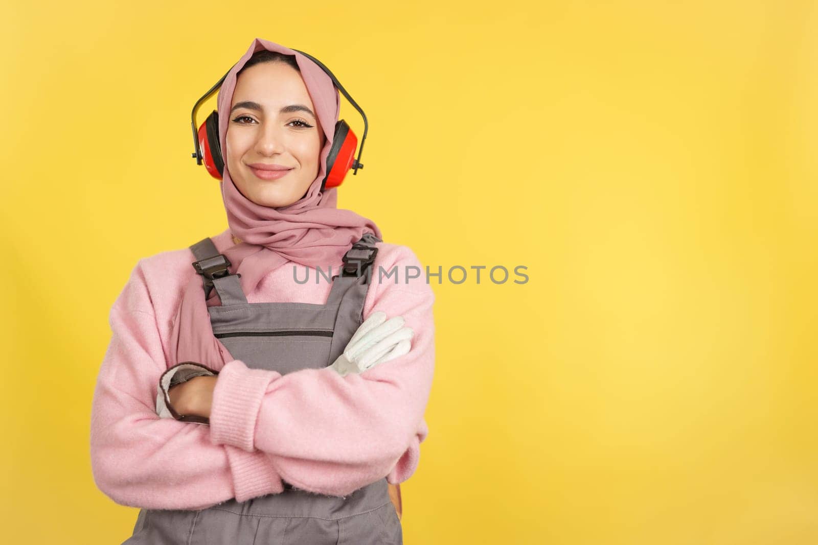 Friendly muslim female carpenter in work uniform looking at camera in studio with yellow background