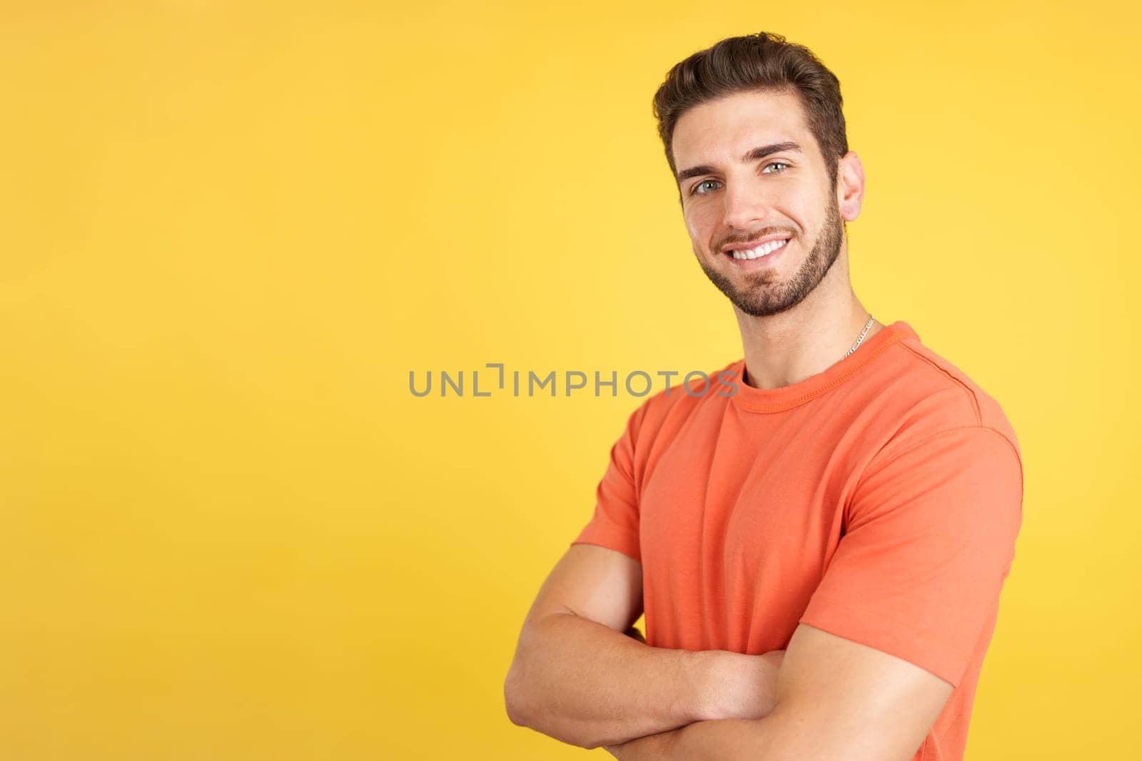 Handsome caucasian man standing whit arms crossed smiling at the camera in studio with yellow background