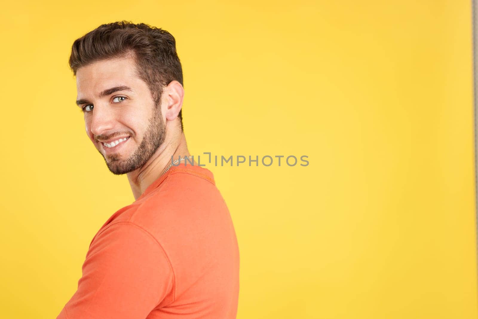 Happy caucasian man turning to smile at the camera in studio with yellow background