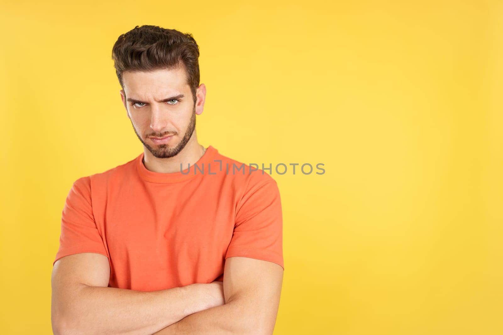 Caucasian man crossing the arms with an angry expression in studio with yellow background