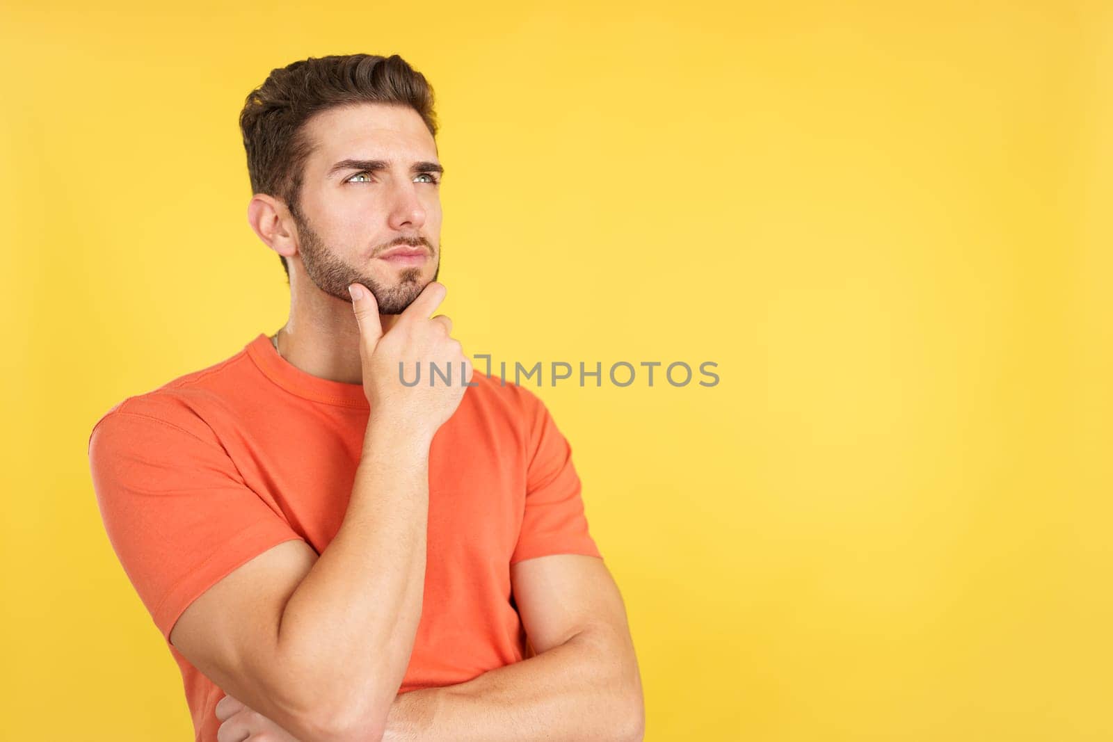 Caucasian man with hand on face and thoughtful expression in studio with yellow background