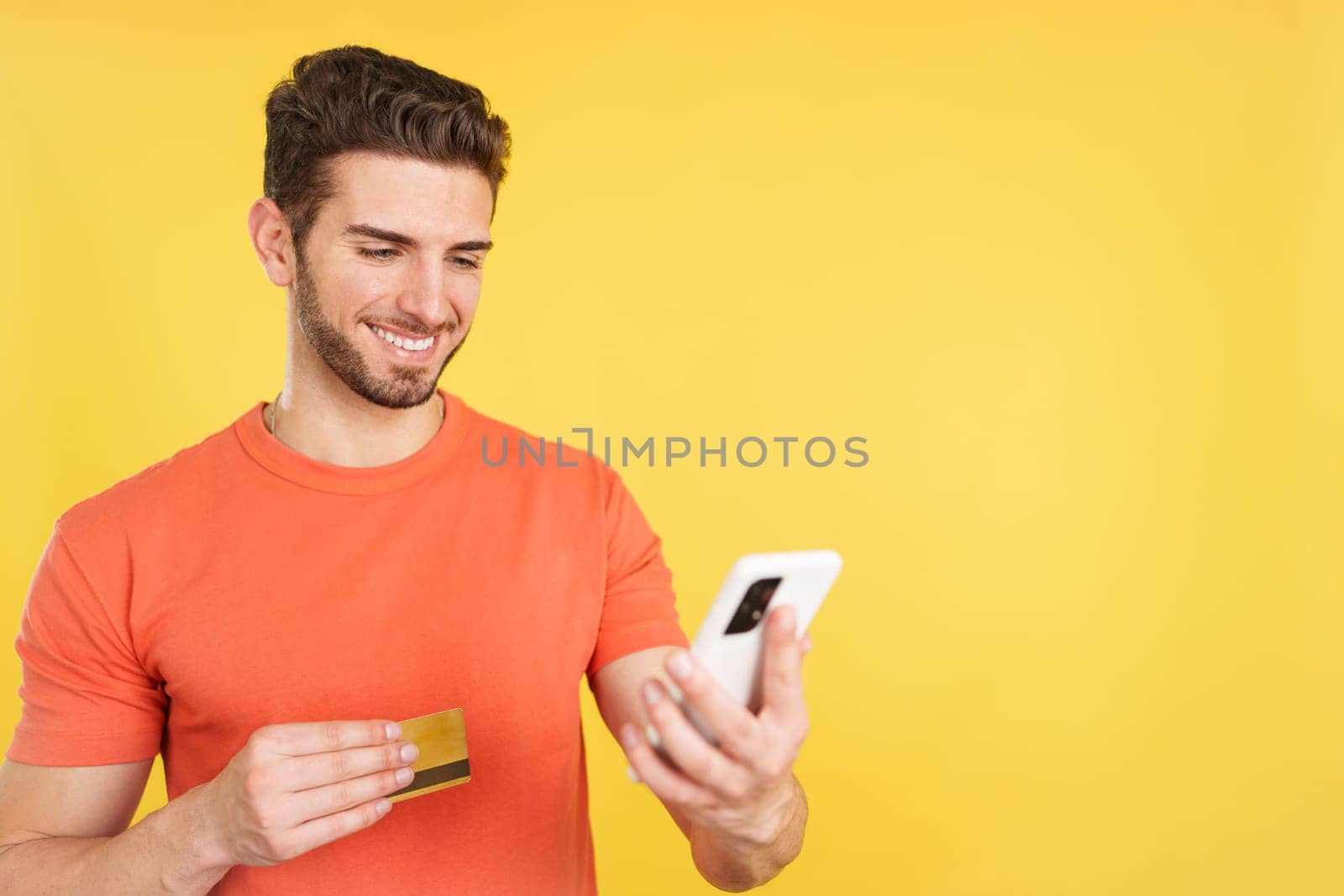 Caucasian man using the mobile and card to shopping online in studio with yellow background