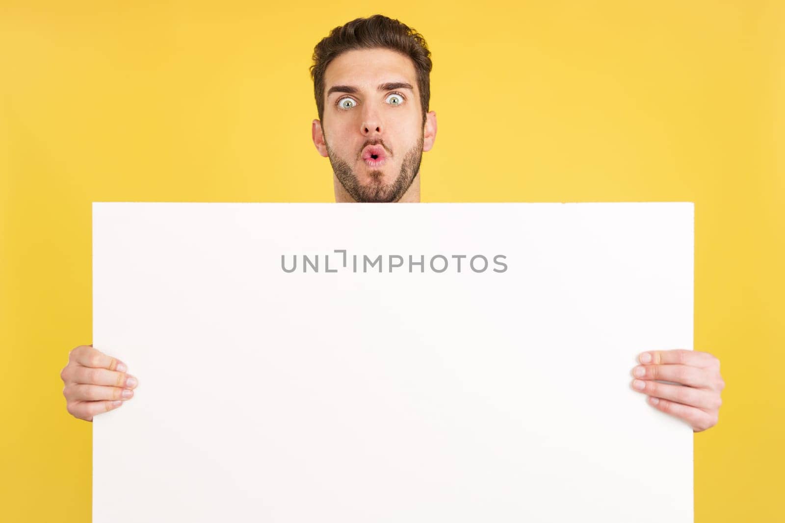 Surprised caucasian man hair holding a blank panel in studio with yellow background