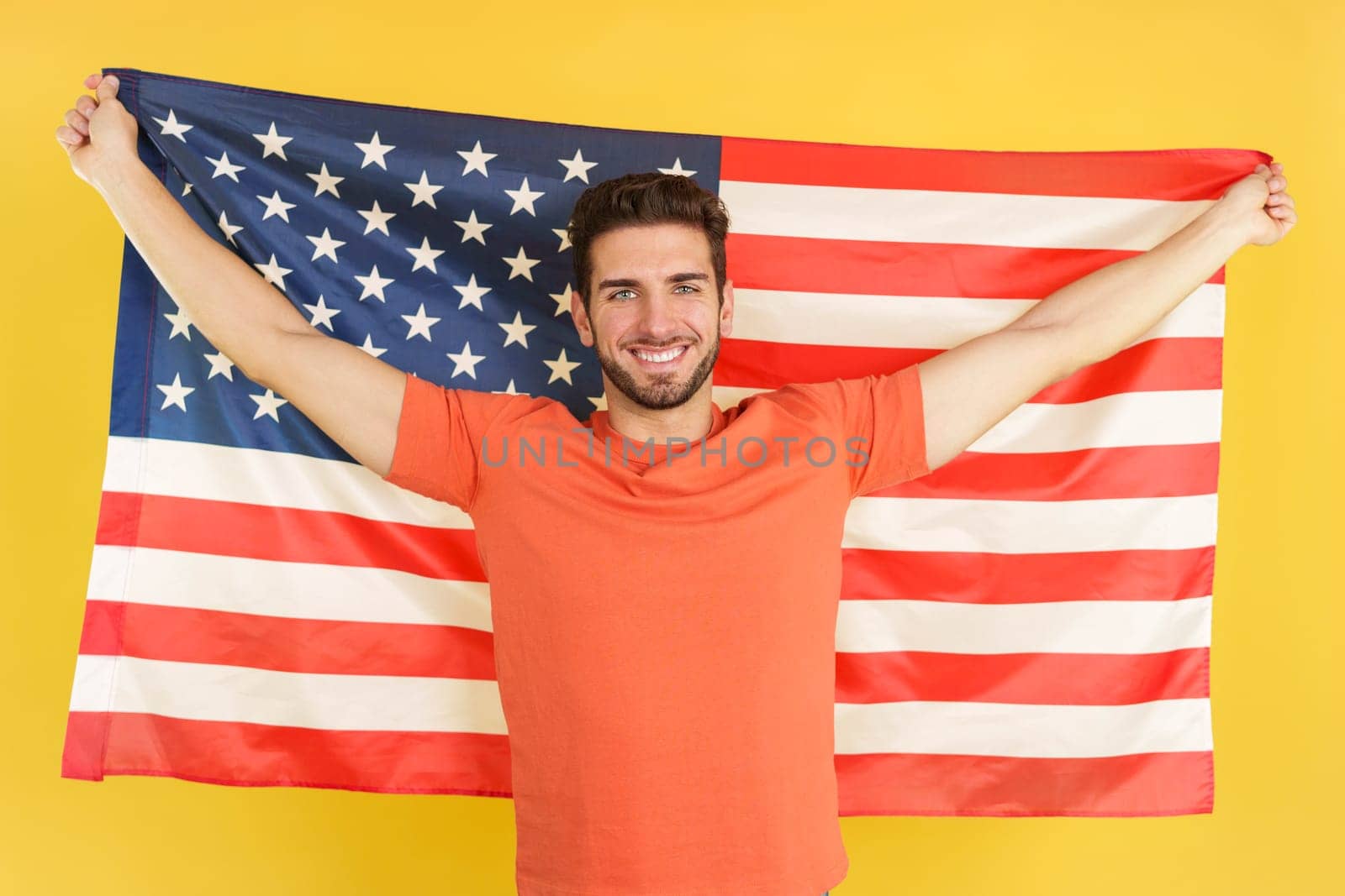Happy caucasian man raising a north america national flag in studio with yellow background