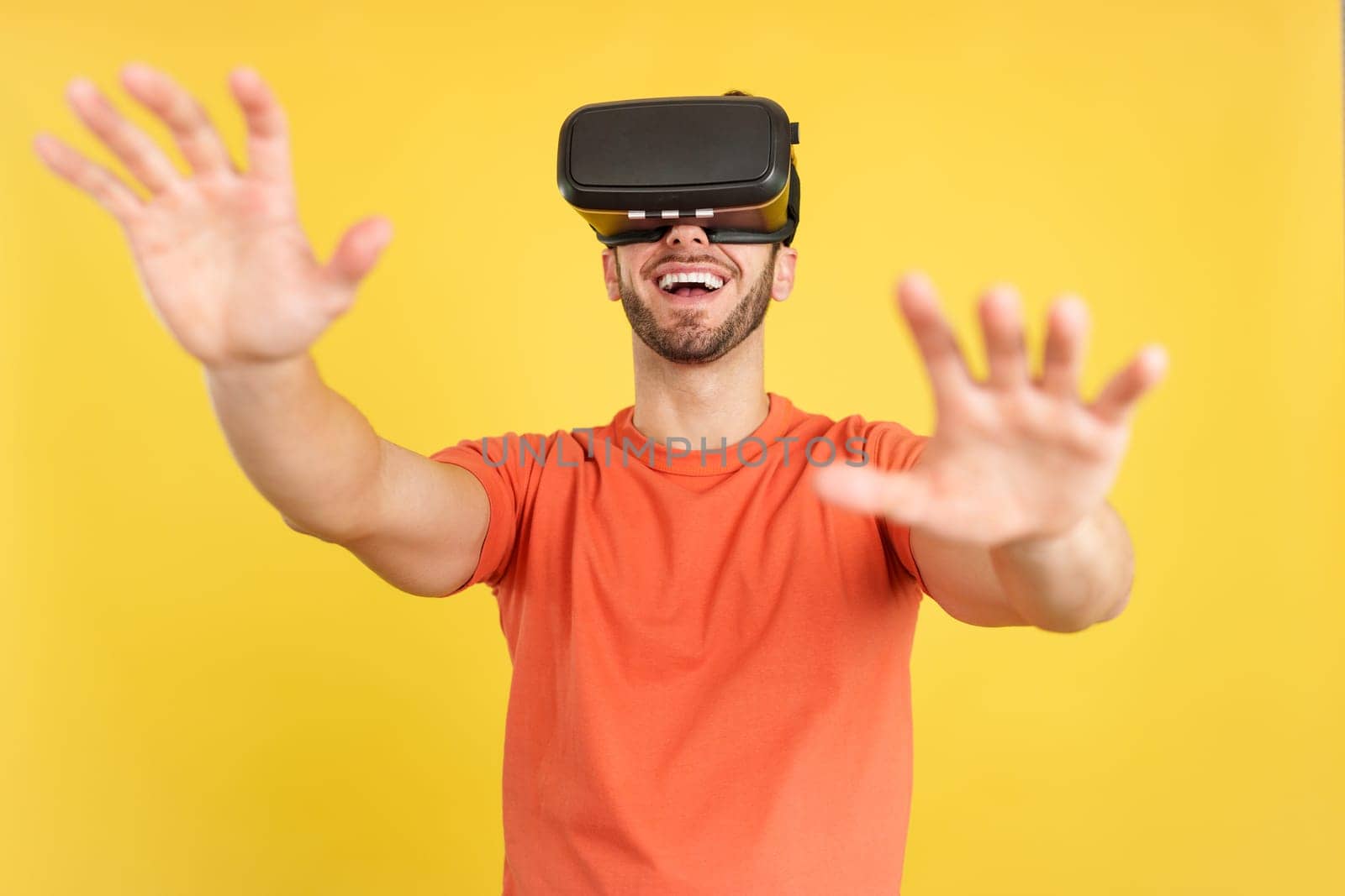 Happy caucasian man with Virtual Reality goggles in studio with yellow background