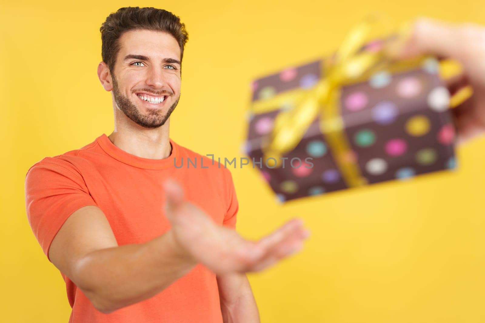 Happy caucasian man smiling while receiving a gift in studio with yellow background