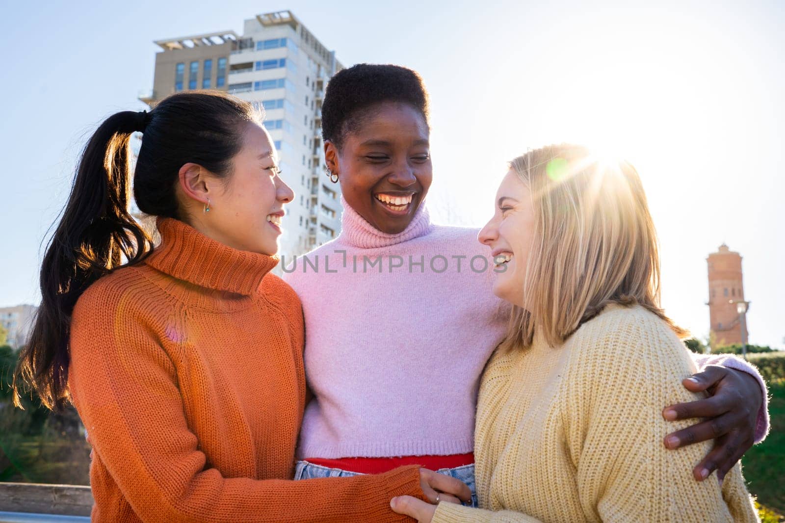 Three female friends affectionately hug each other having fun together laughing happy smiling. Collective lovely embrace concept.