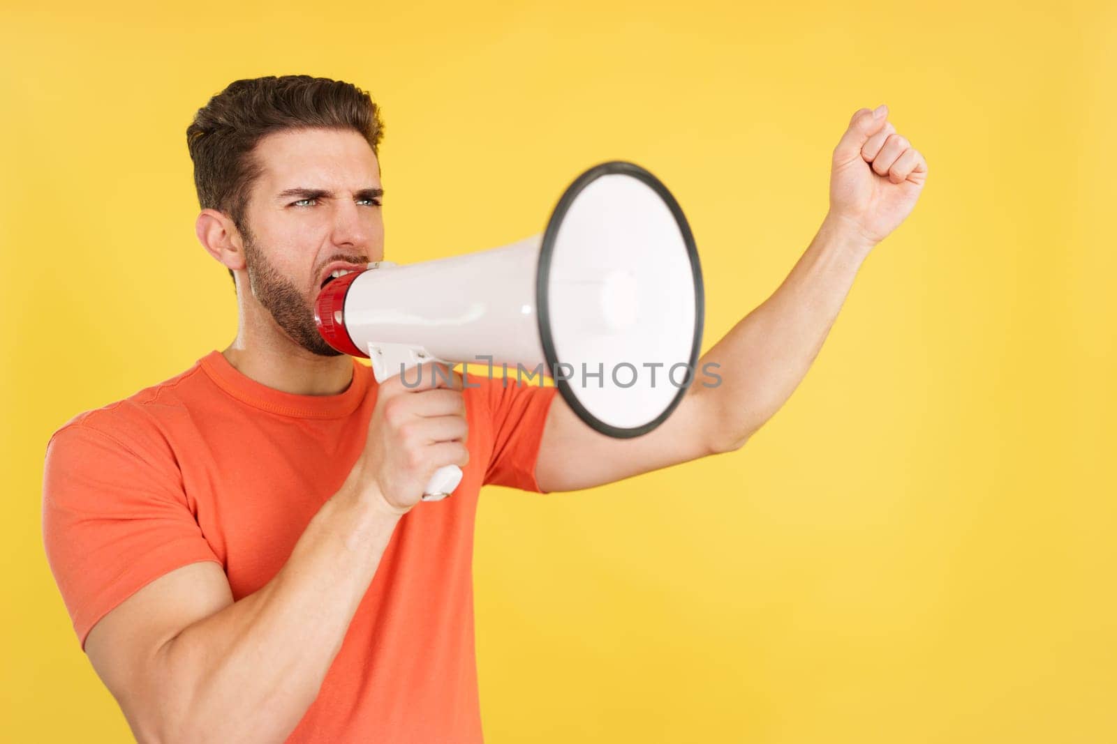 Angry caucasian man shouting using a loudspeaker in studio with yellow background