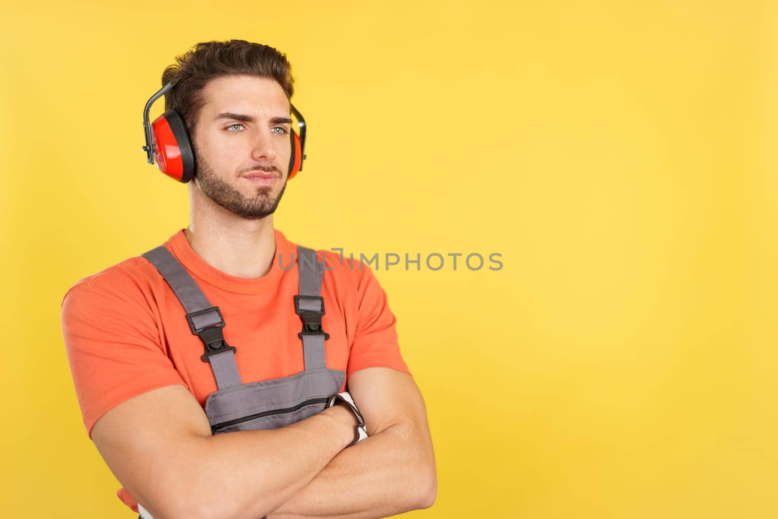 Serious worker with headphones standing looking aside in studio with yellow background