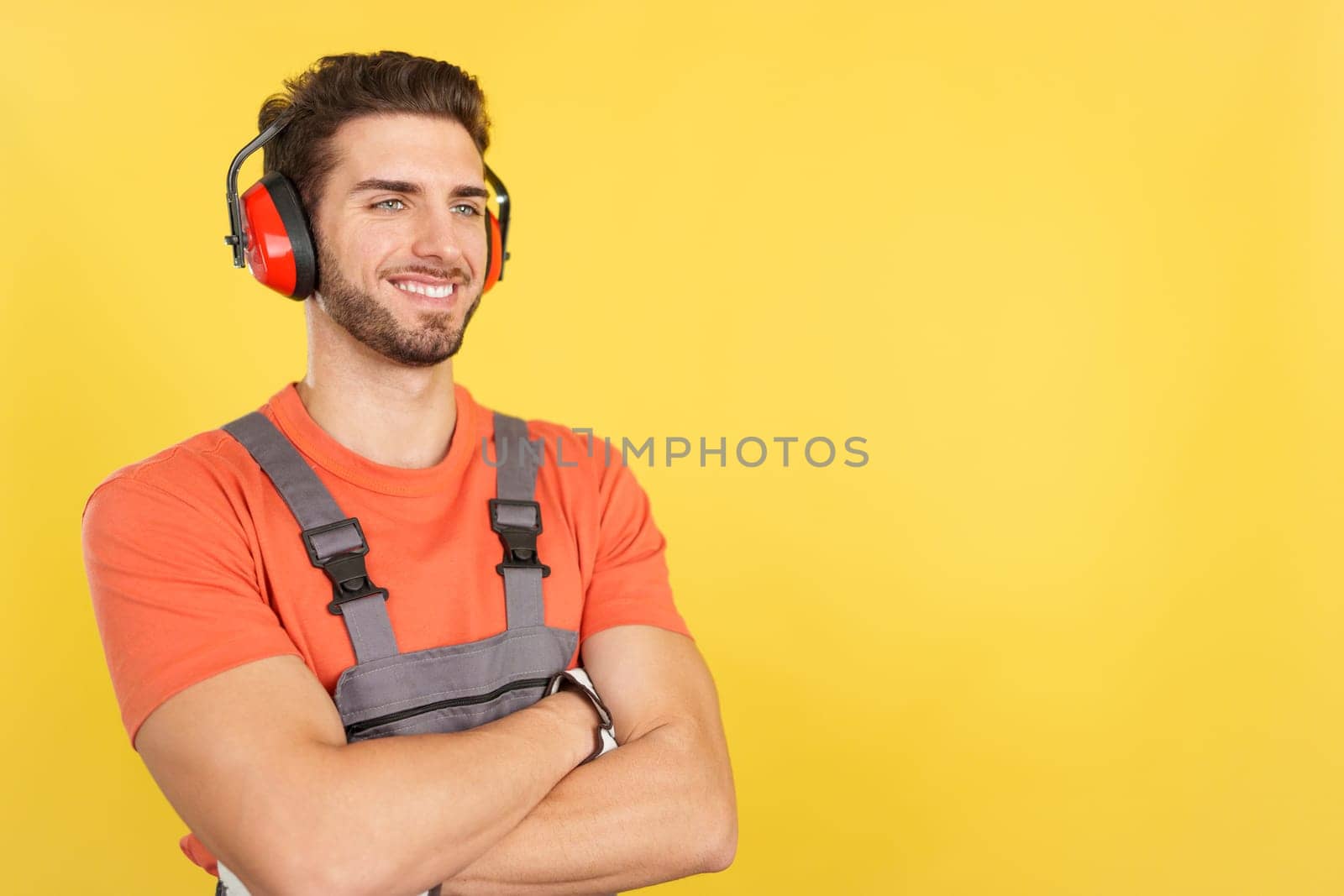 Distracted caucasian male carpenter looking away with arms crossed in studio with yellow background