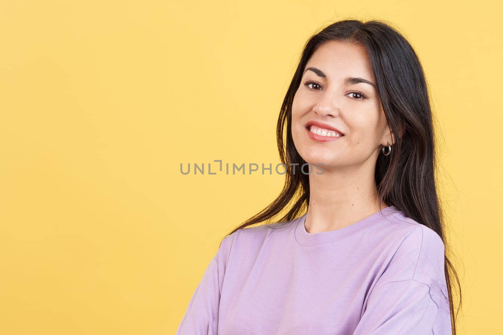 Happy hispanic woman smiling at the camera in studio with yellow background