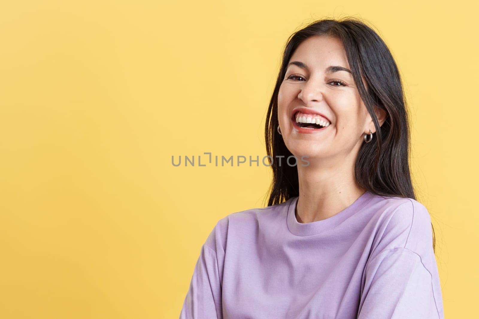 Happy hispanic woman laughing and looking at the camera in studio with yellow background