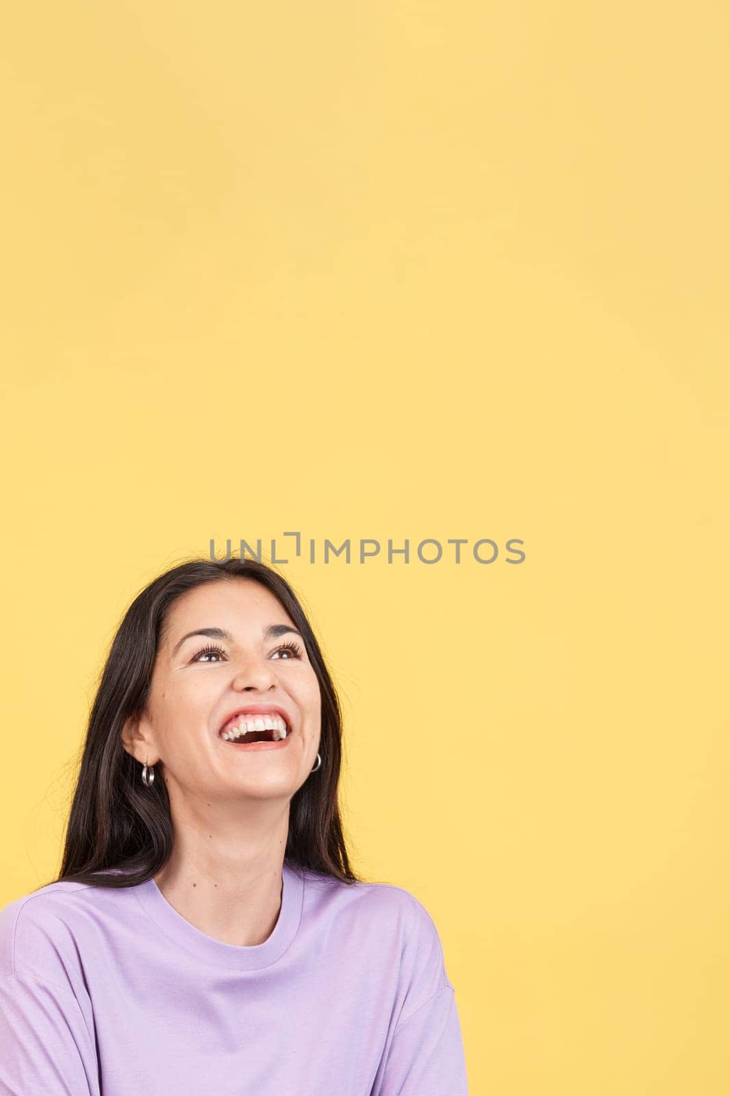 Hispanic woman laughing and looking up in studio with yellow background