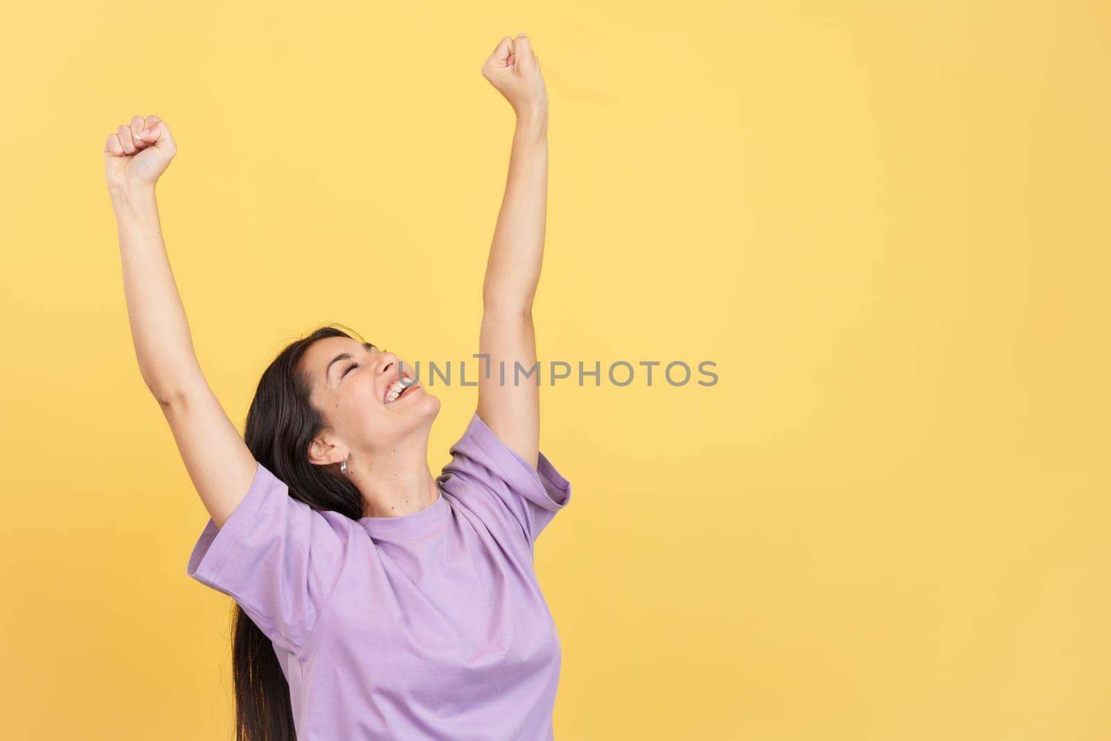 Happy caucasian woman celebrating while raising arms in studio with yellow background