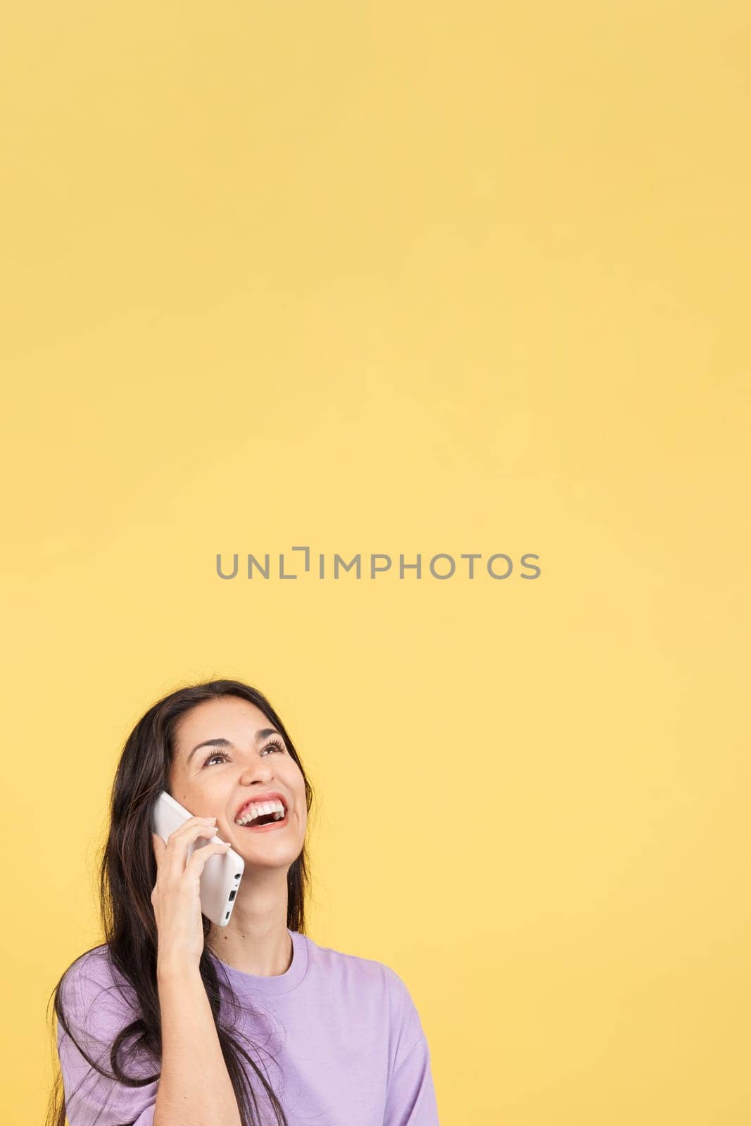 Happy hispanic woman smiling while talking to the mobile in studio with yellow background