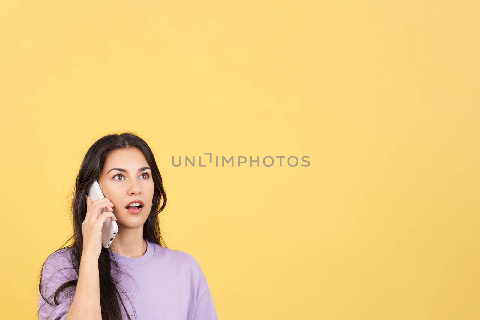 Surprised hispanic woman talking to the mobile in studio with yellow background