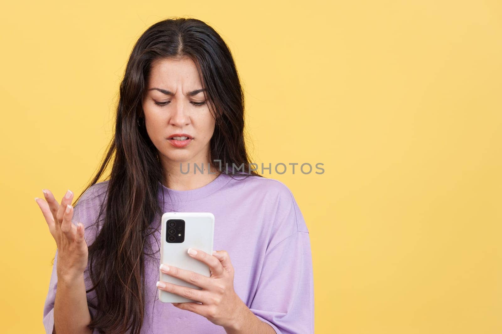 Worried caucasian woman using a mobile phone in studio with yellow background