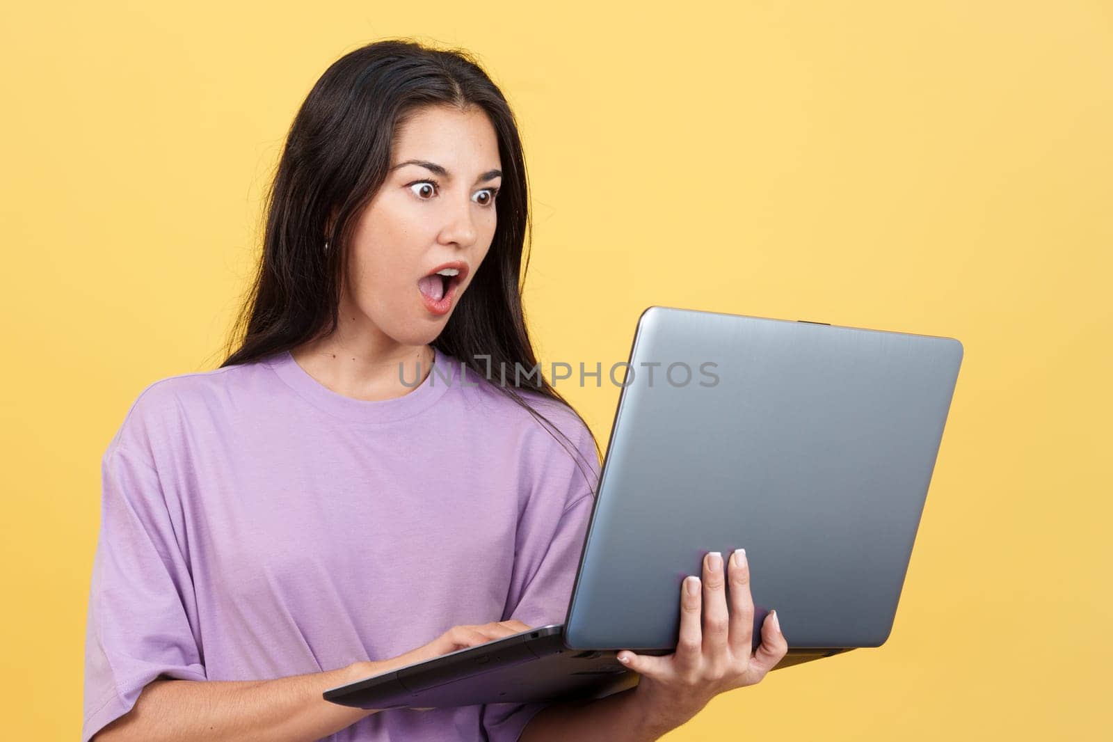 Caucasian woman with a surprised look using a laptop in studio with yellow background