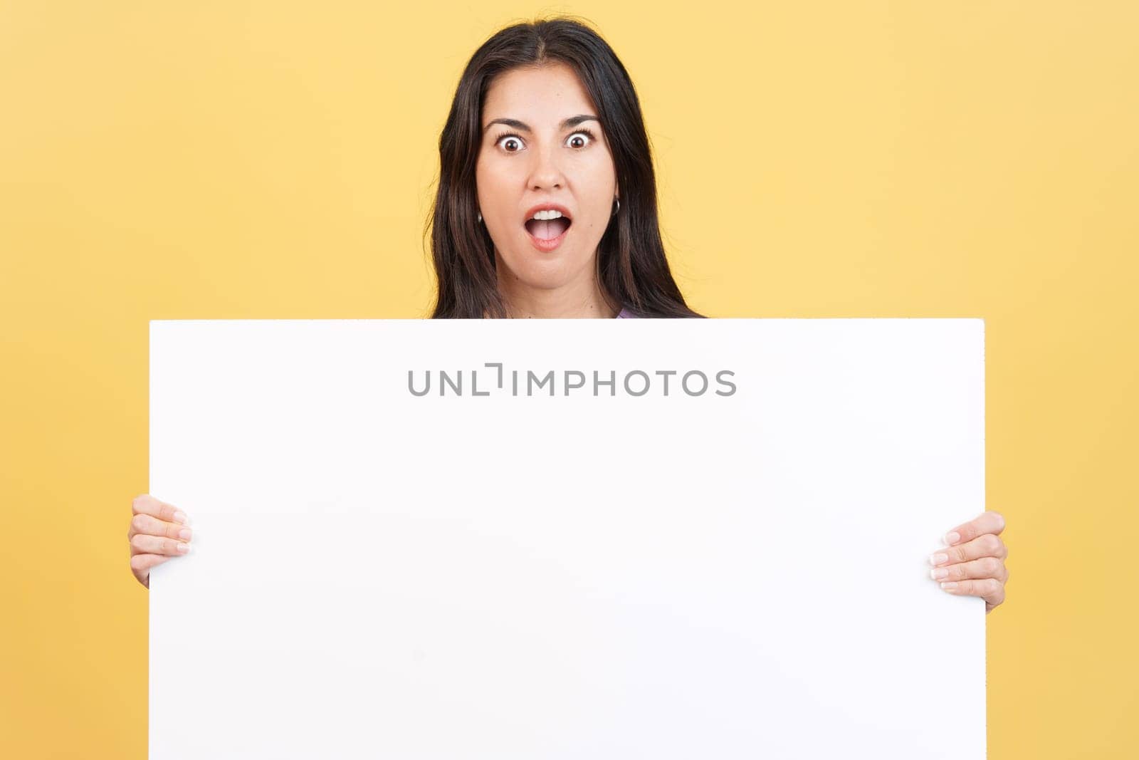 Amazed caucasian woman hair holding a blank panel in studio with yellow background