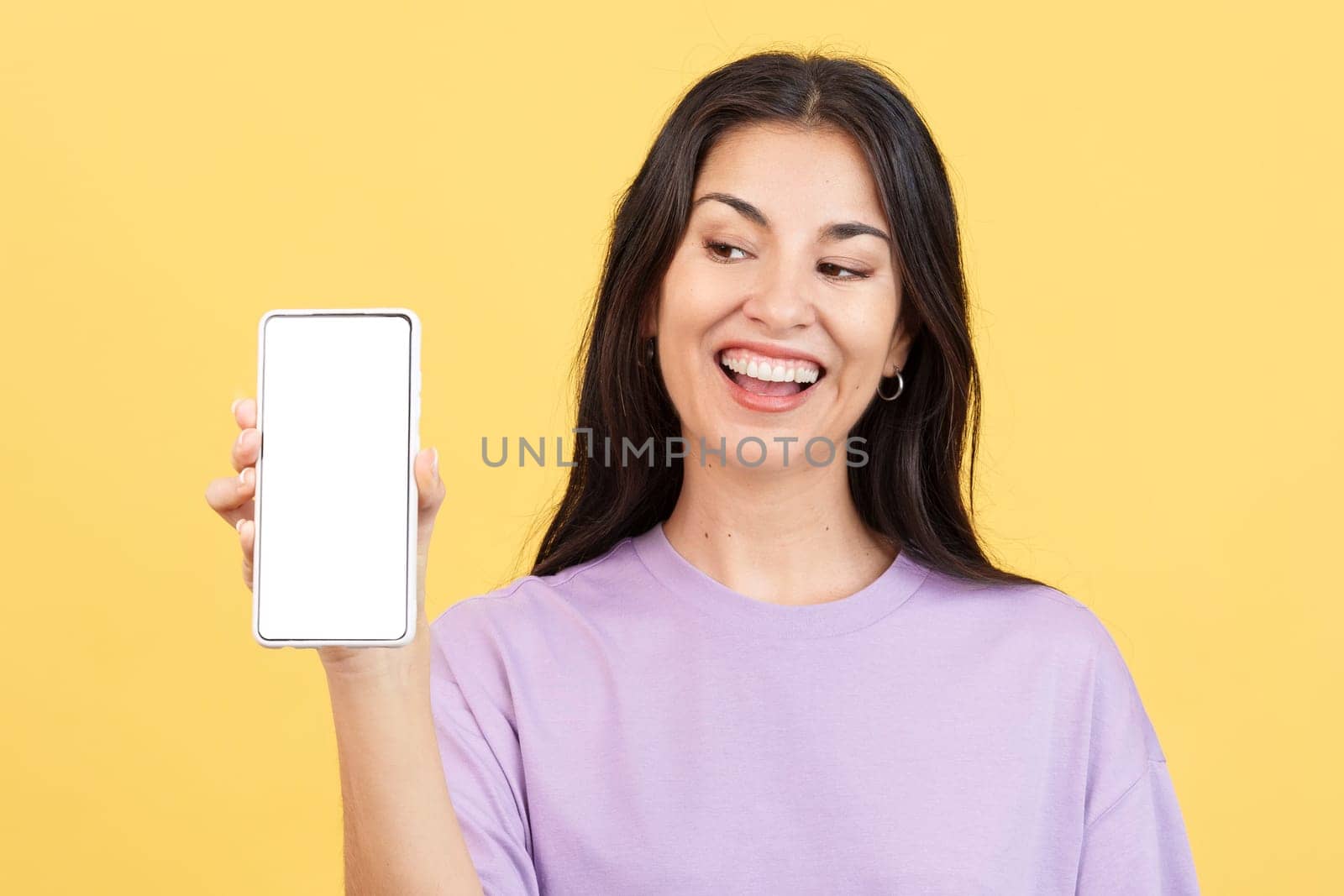 Amazed woman holding a mobile with a blank screen in studio with yellow background