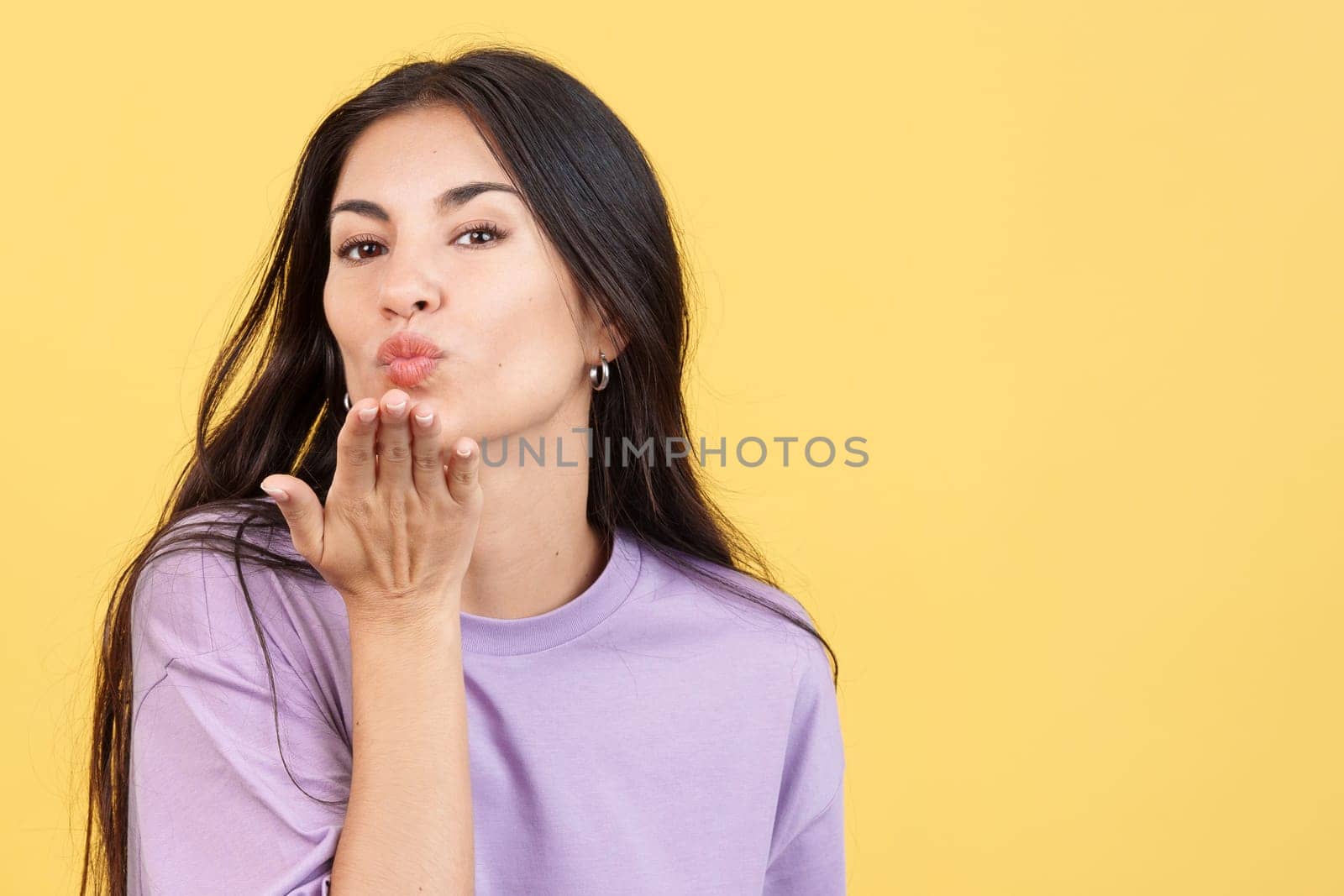 Woman blowing a kiss while looking at the camera in studio with yellow background
