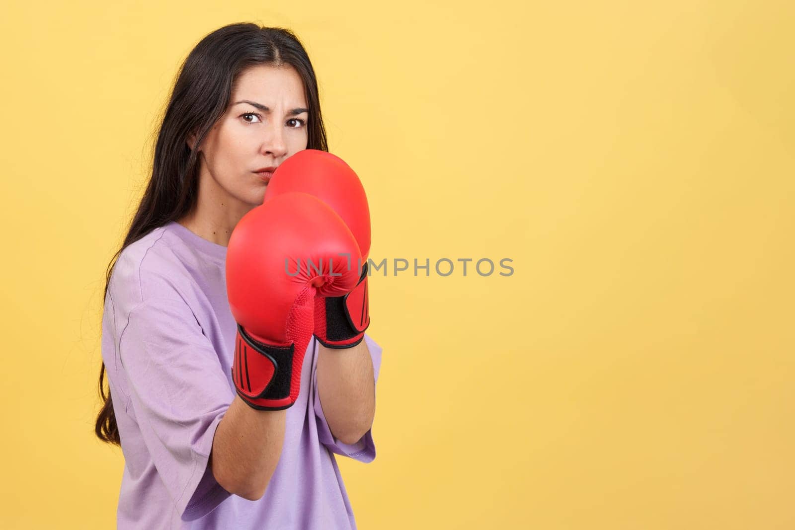Caucasian woman with boxing gloves in fight pose with yellow background
