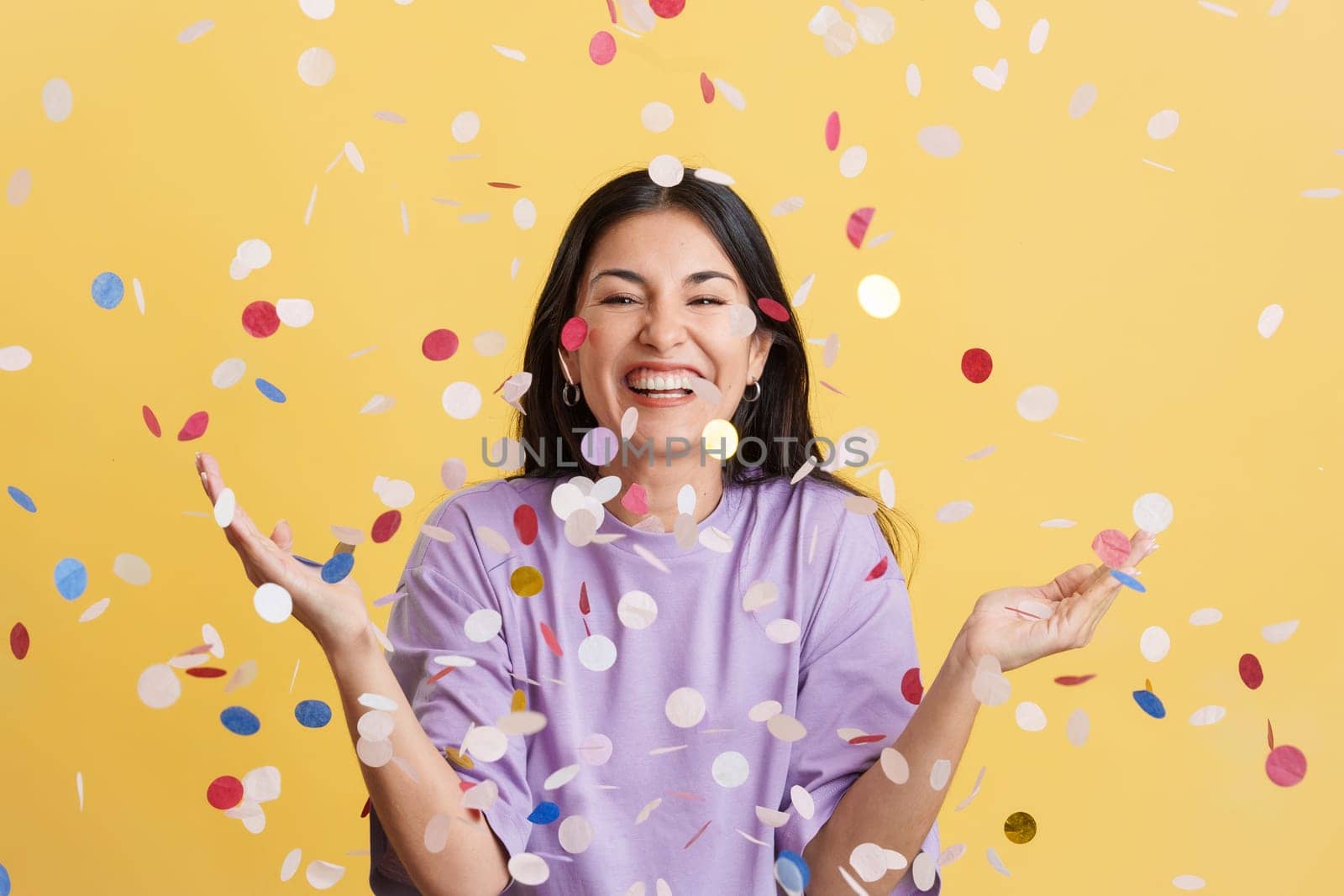 Happy woman surrounded by confetti flying in the air in studio with yellow background