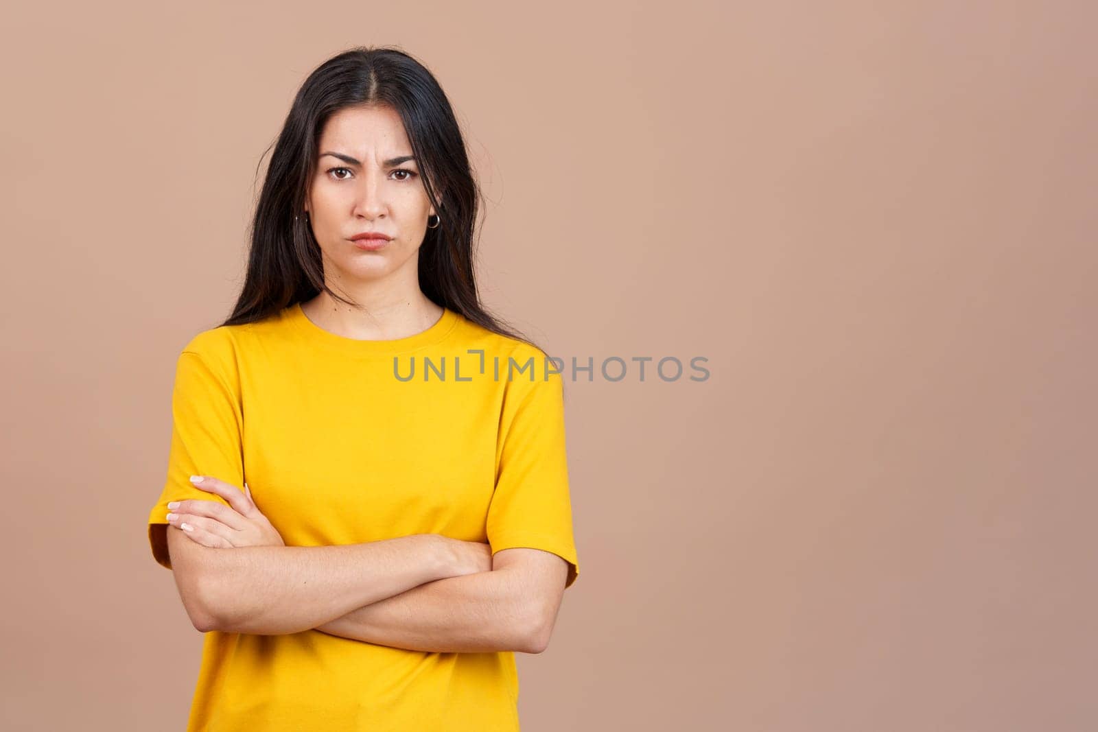 Hispanic woman crossing the arms with an angry expression in studio with brown background