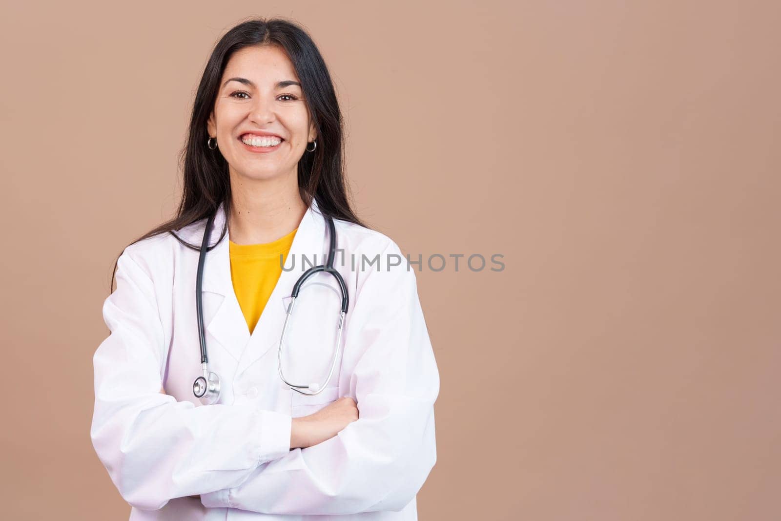 Caucasian female doctor smiling at the camera with arms crossed in studio with brown background