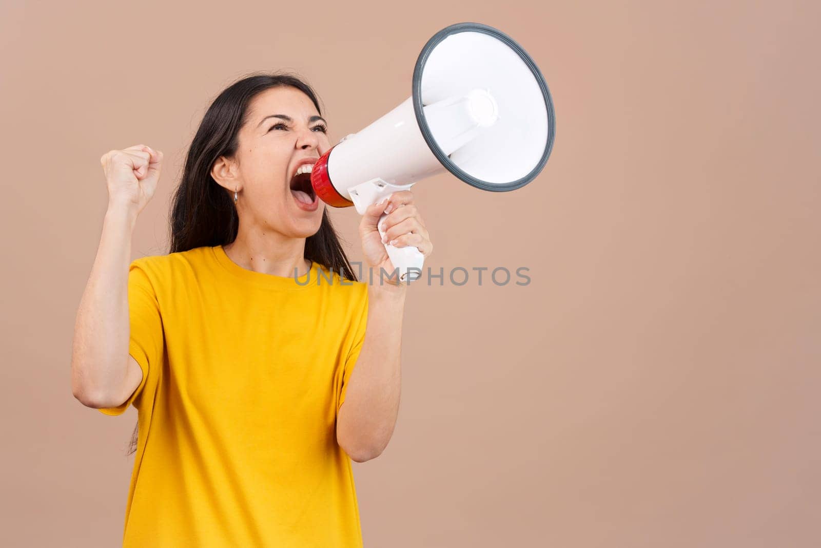 Upset caucasian woman yelling using a loudspeaker in studio with brown background