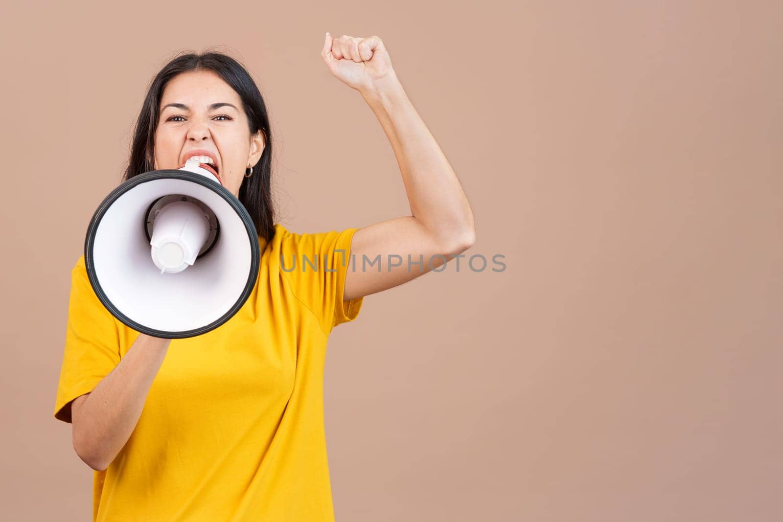 Angry caucasian woman shouting using a loudspeaker in studio with brown background