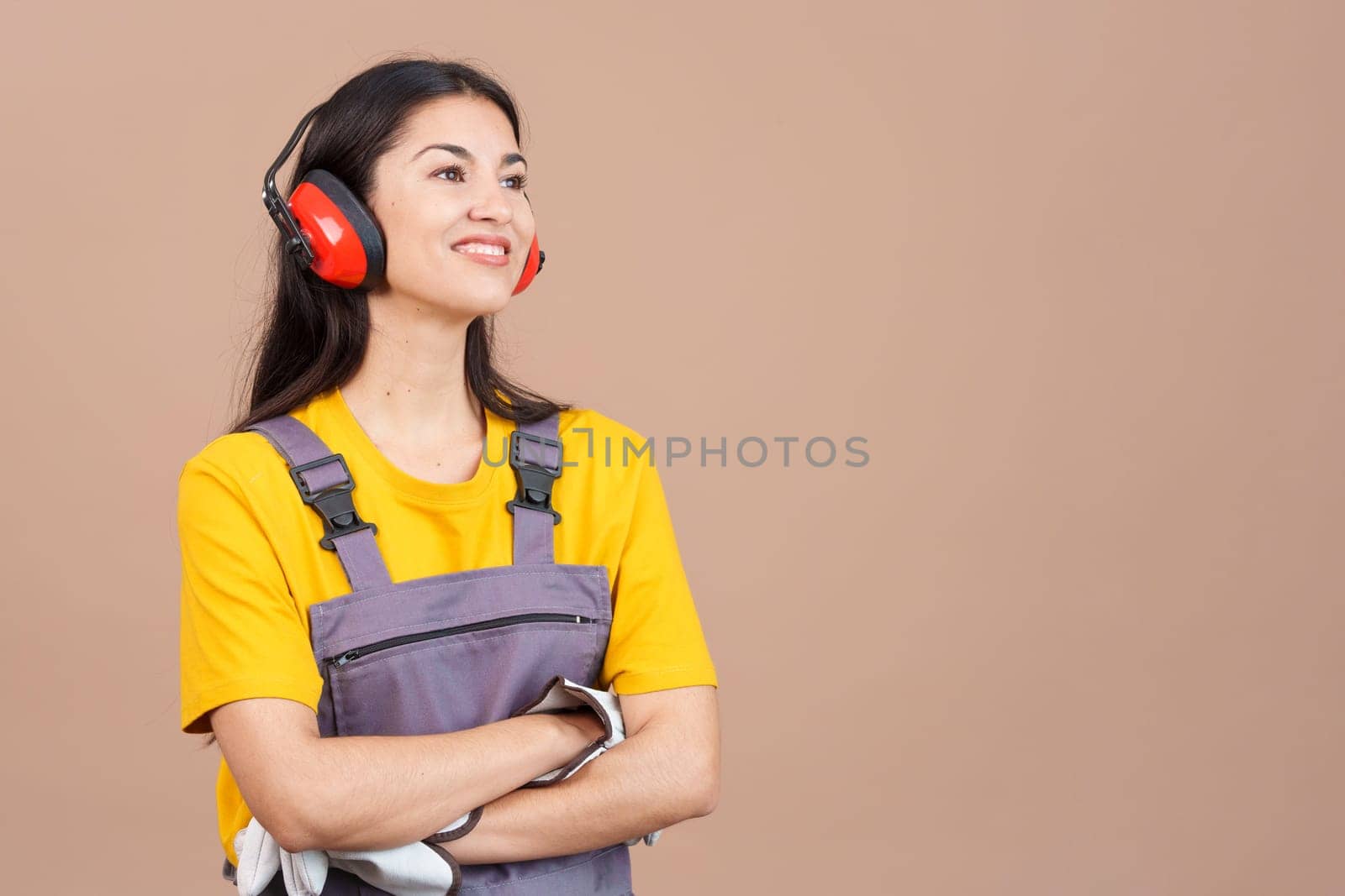 Distracted female carpenter looking away with arms crossed in studio with brown background