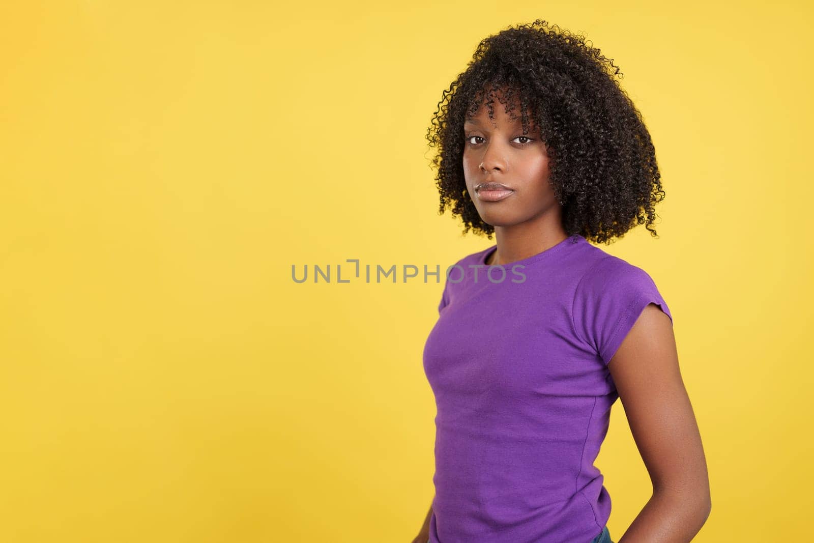 Serious woman with afro hair looking at camera in studio with yellow background