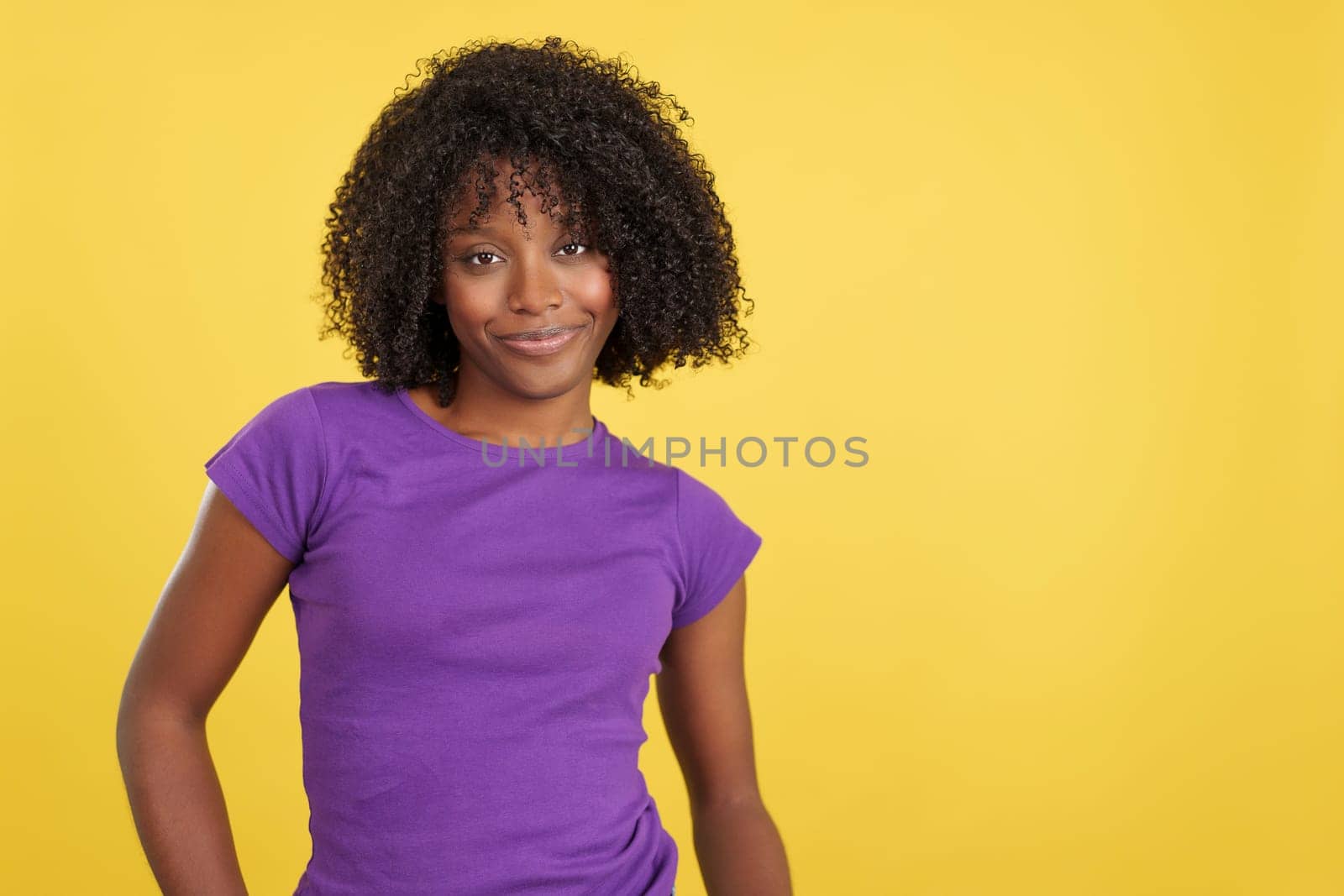 Woman with afro hair smiling at camera in studio with yellow background