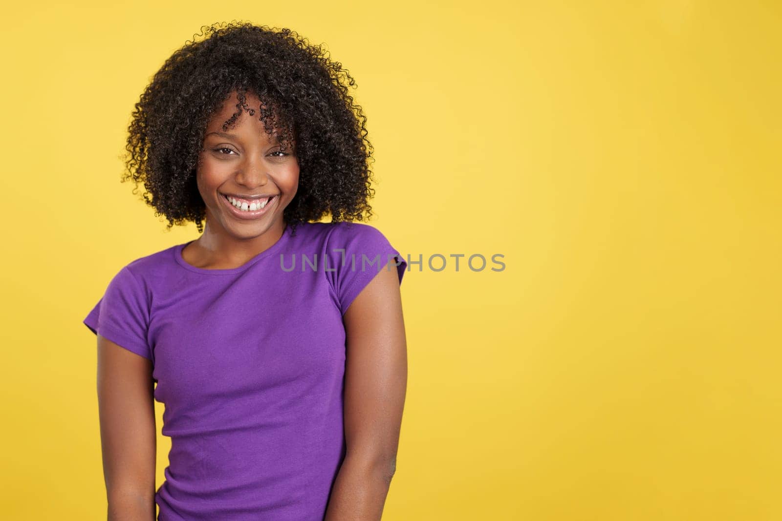 Cool woman with afro hair laughing while looking at camera in studio with yellow background