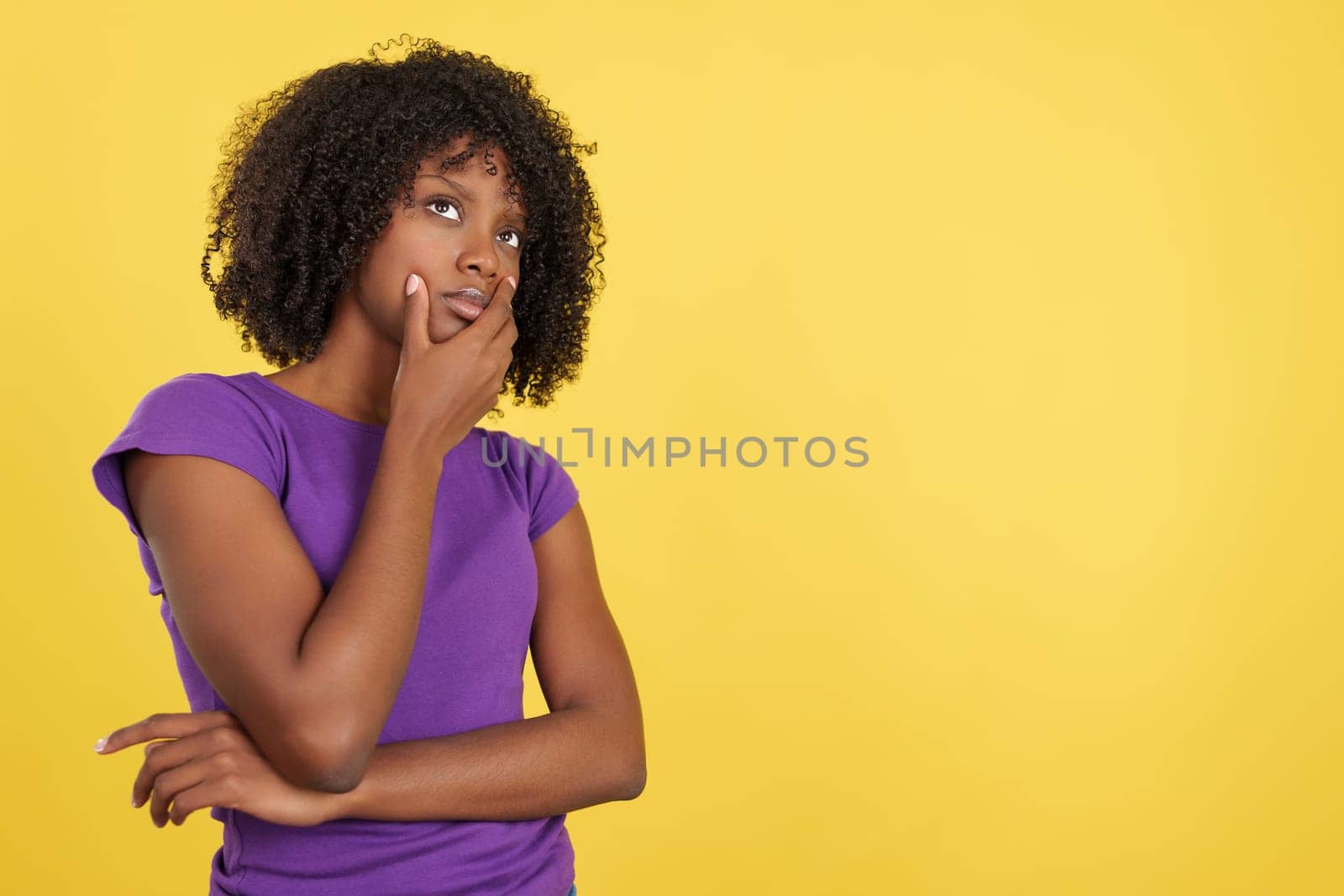 Woman with afro hair standing with thoughtful expression in studio with yellow background