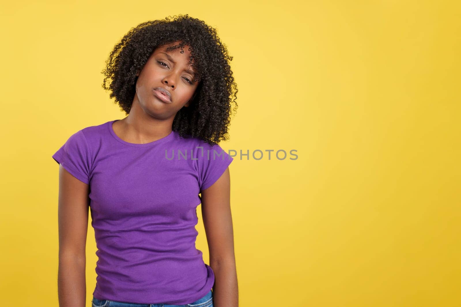 Woman with African hair standing in discomfort in studio with yellow background