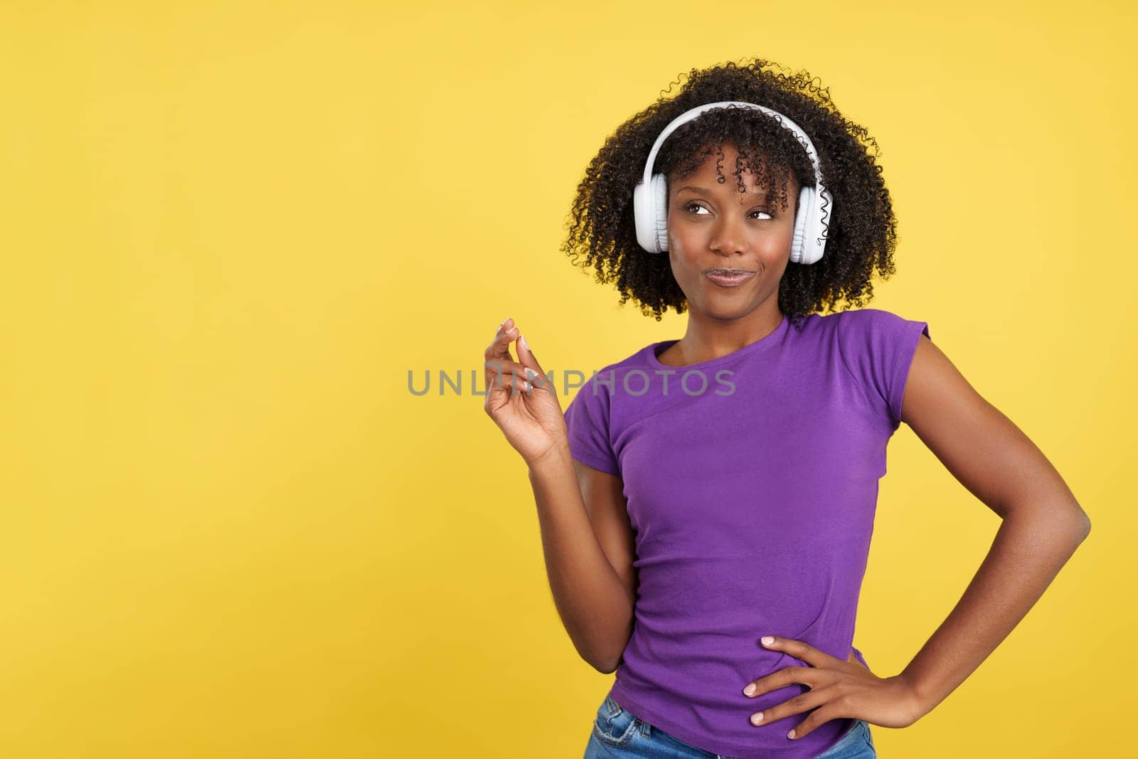 Cool beauty woman with afro hair listening to music with headphones in studio with yellow background