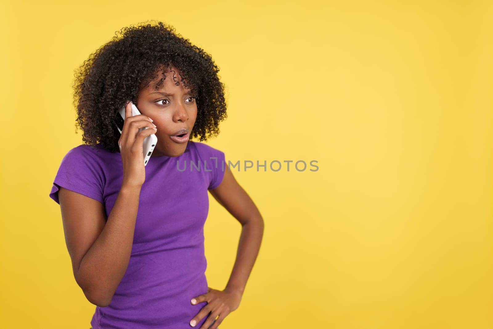 Woman with afro hair talking to the mobile with angry expression in studio with yellow background