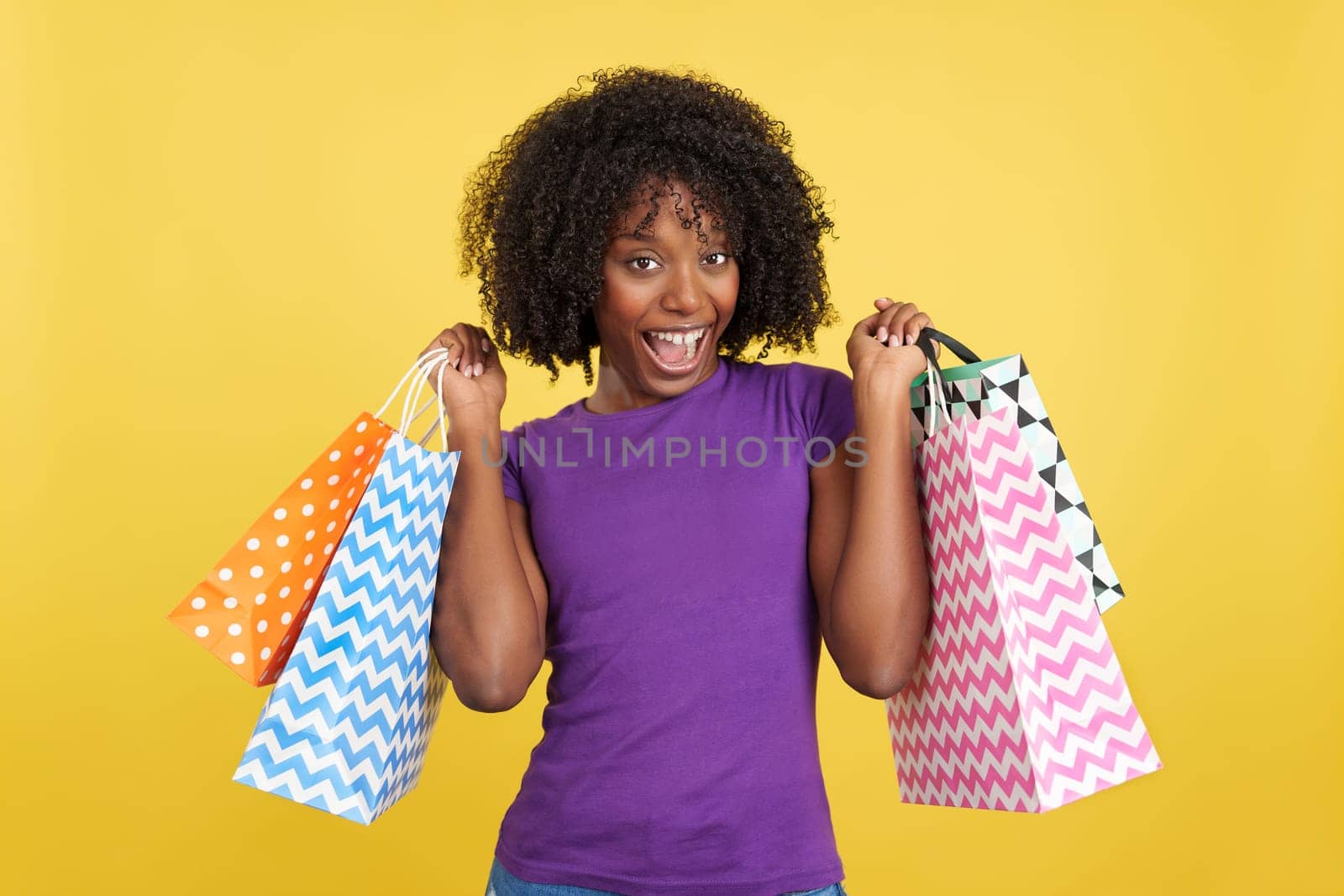 Happy woman with curly hair holding shopping bags in studio with yellow background