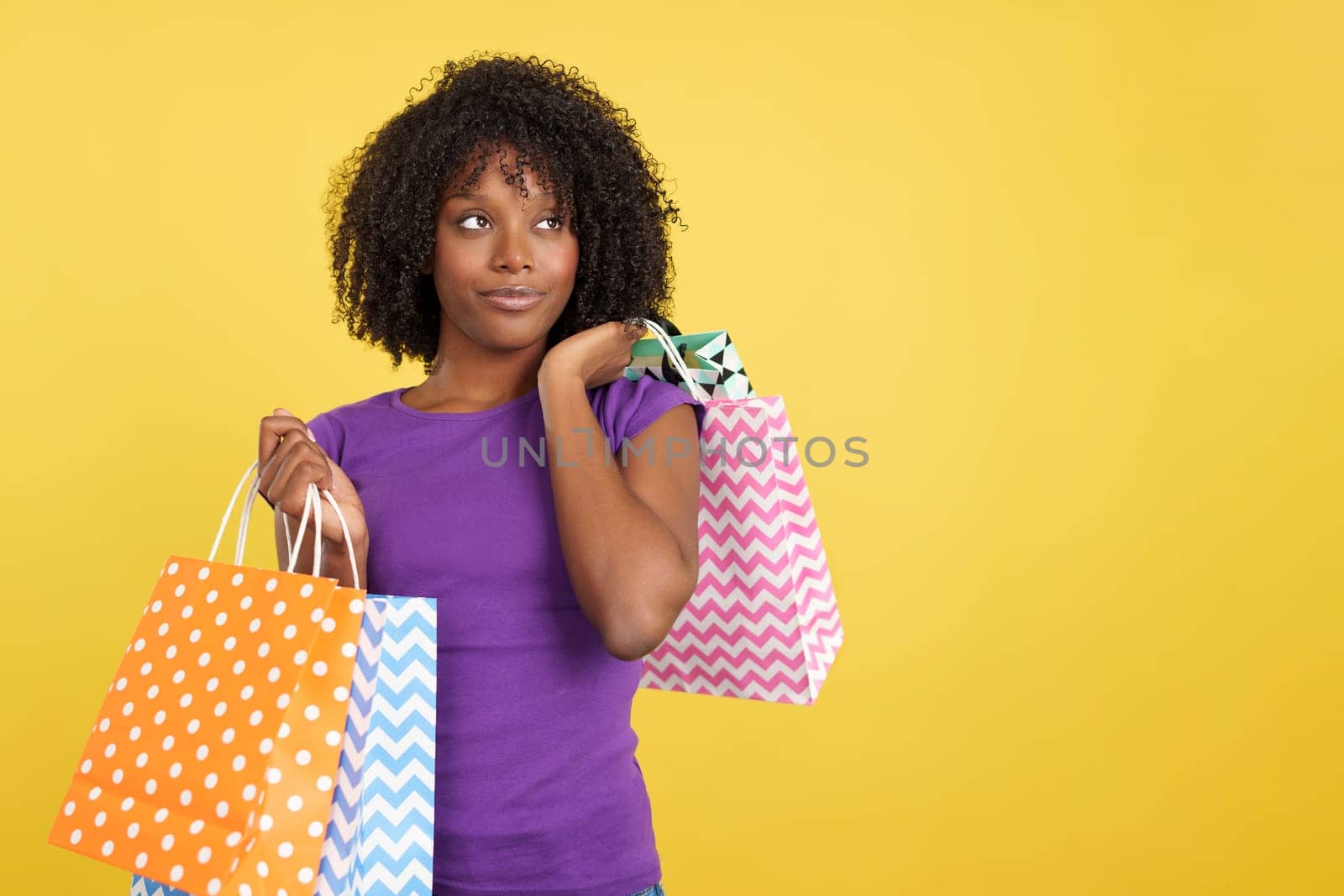 Cool woman with afro hair and shopping bags in studio with yellow background